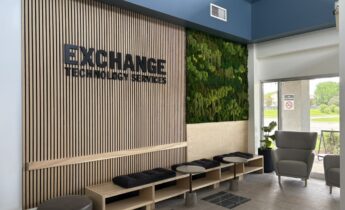 Exchange Technology Services office lobby with branded wood slat wall, bench seating, small tables, grey chairs, and a green moss wall installation.